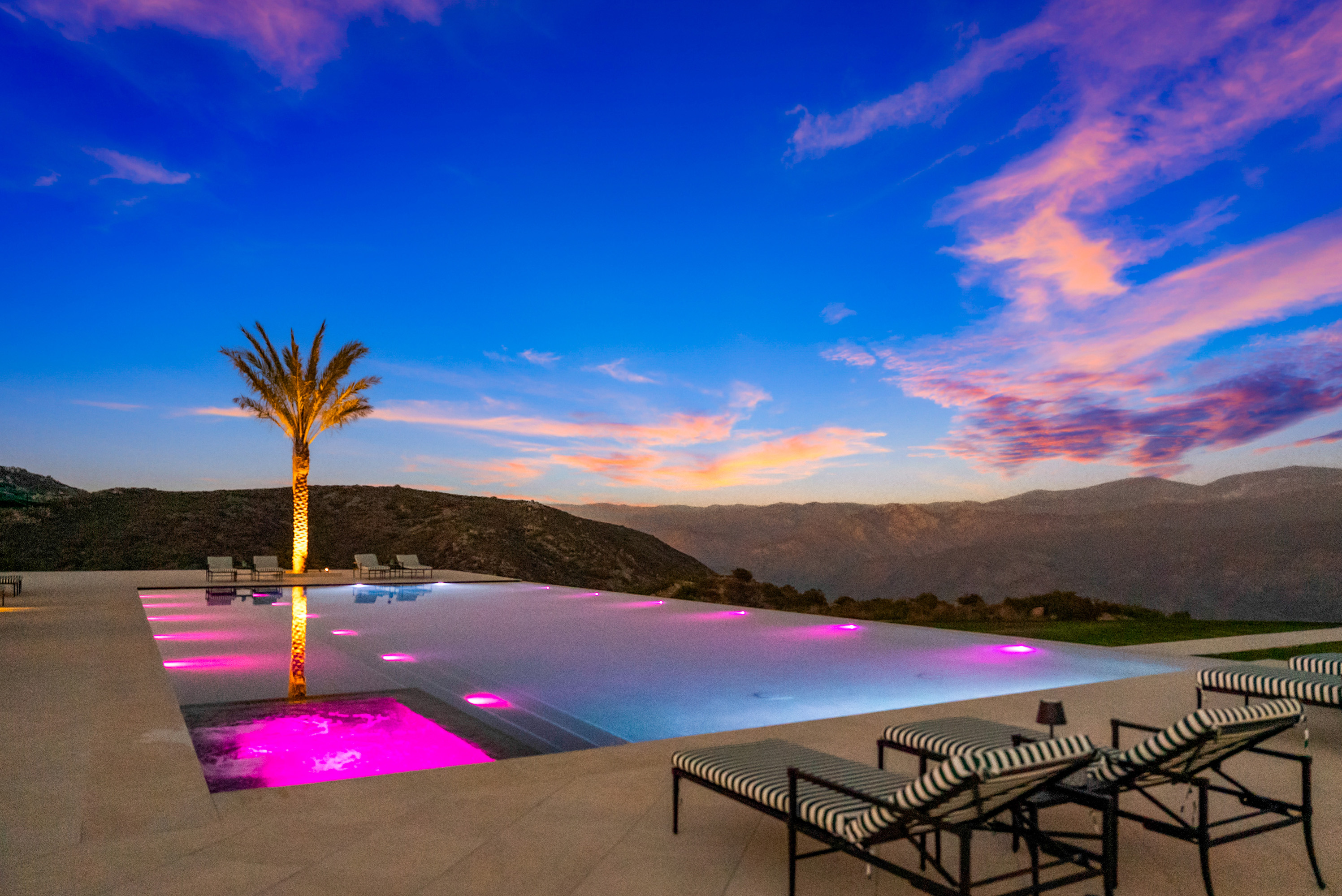 Infinity pool at sunset with lit water and mountain silhouettes